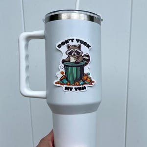 Sticker on white tumbler. Sticker pictures cute raccoon in trash can with the words "Don't Yuck My Yum".