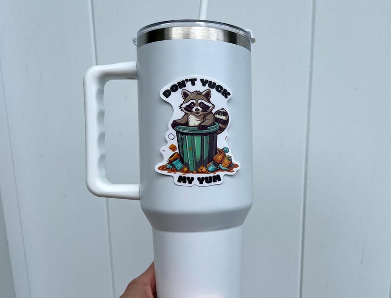 Sticker on white tumbler. Sticker pictures cute raccoon in trash can with the words "Don't Yuck My Yum".