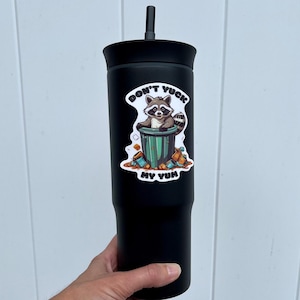 Sticker on black tumbler. Stick pictures cute raccoon in trash can with the words "Don't Yuck My Yum".