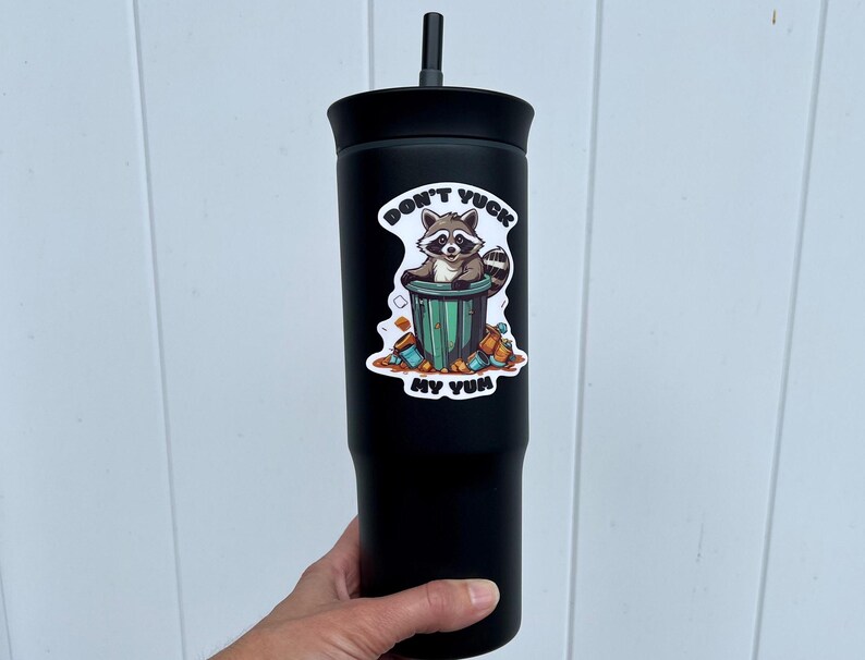 Sticker on black tumbler. Stick pictures cute raccoon in trash can with the words "Don't Yuck My Yum".