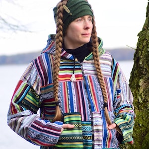 May include: A colorful patchwork jacket with a hood and zipper closure. The jacket features a vibrant mix of vertical stripes in various colors, including red, blue, green, and white. The person is wearing a green beanie and has long braids.