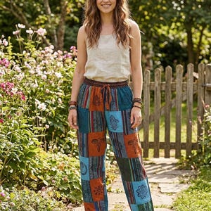 Könnte beinhalten: Eine Person trägt ein beiges Tanktop und eine Patchworkhose mit Kordelzug. Die Hose hat eine Mischung aus blauen, orangefarbenen und grünen Quadraten mit verschiedenen Druckmustern. Die Szene spielt in einem Garten.