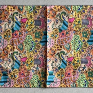 May include: A patterned table runner in shades of yellow, pink, blue, and green, featuring a paisley design. The runner has tassels at each end. The fabric is decorated with floral and abstract shapes.