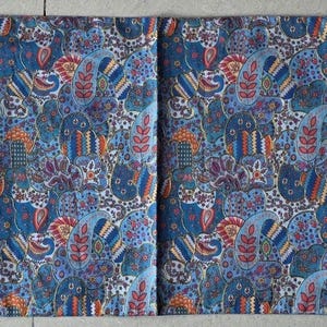 May include: A long, rectangular table runner with a blue, red, and white paisley pattern. The runner has a pointed end on each side with a tassel. The runner is made of fabric and is designed to be placed on a table.