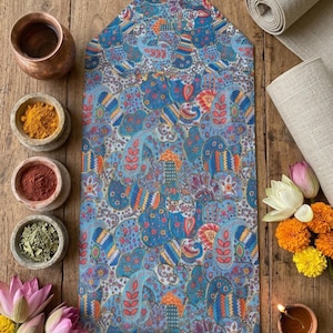 Puede incluir: Un camino de mesa azul con estampado de cachemira y una borla decorativa. El camino de mesa está rodeado de cuencos con especias, flores y tela enrollada sobre una superficie de madera. El diseño del camino de mesa incluye detalles en azul, naranja y rojo.