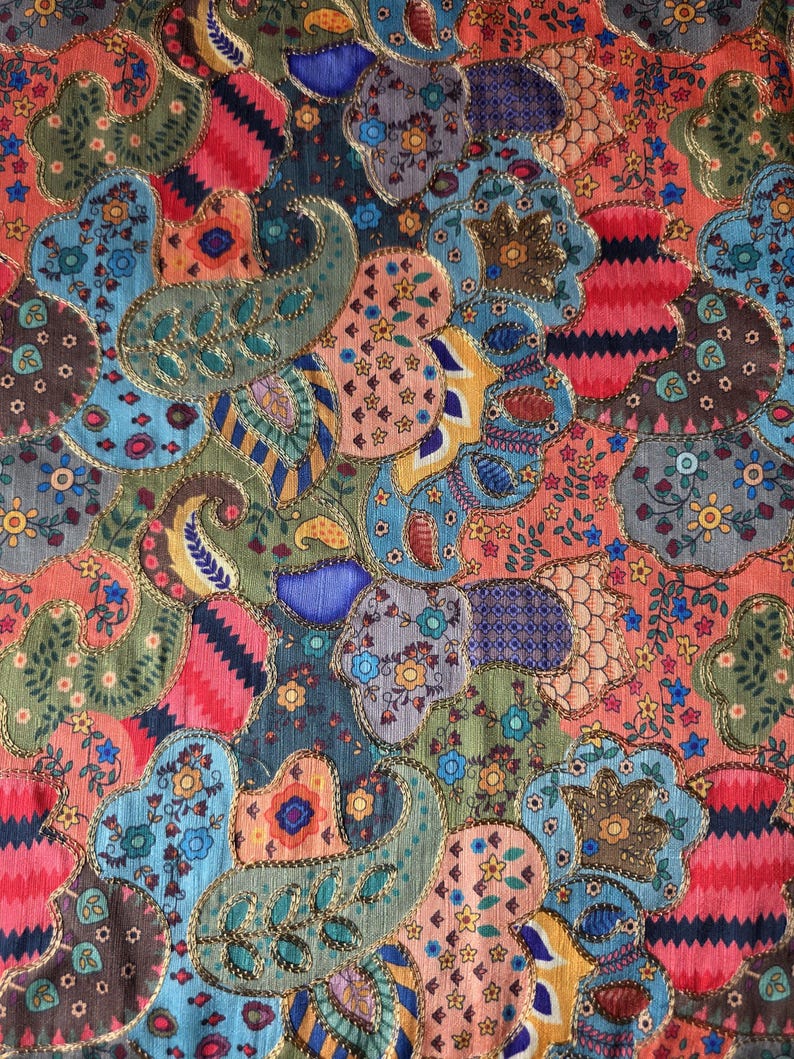 May include: A vibrant textile with a patchwork design. The fabric showcases paisley and floral patterns in blue, green, red, and orange, edged with gold trim. The overall design is intricate and detailed, with a rich, textured appearance.
