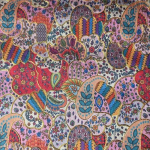 May include: A colourful textile with a paisley design in shades of pink, red, orange, blue, and green. The pattern includes floral and leaf elements, edged with gold trim. The fabric has a detailed, ornate appearance, suitable for various craft projects.