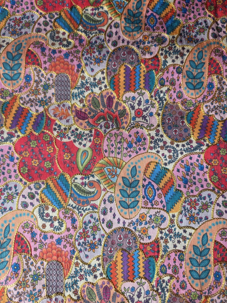 May include: A colourful textile with a paisley design in shades of pink, red, orange, blue, and green. The pattern includes floral and leaf elements, edged with gold trim. The fabric has a detailed, ornate appearance, suitable for various craft projects.