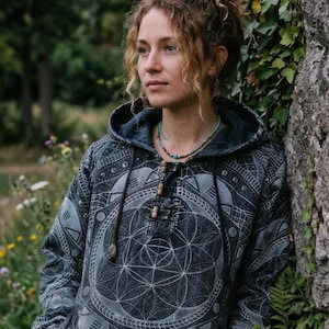 May include: A charcoal grey hooded pullover featuring a white geometric pattern of circles and lines across the front. The garment includes a drawstring hood with wooden beads, long sleeves, and front pockets, crafted from a textured fabric.