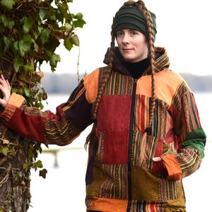 May include: A hooded patchwork jacket in shades of orange, red, green, and brown. The jacket has a zip and pockets. The design incorporates various patterns and textures, creating a unique and bohemian style. A green hat is also visible.