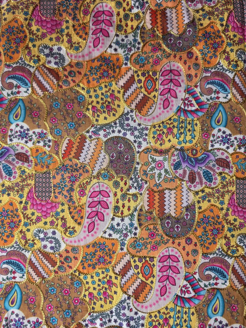 May include: A colourful textile with a patchwork design. The fabric features paisley and floral patterns in shades of gold, orange, pink, yellow, and brown. The design is outlined with gold trim, creating a visually appealing pattern.
