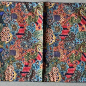 May include: A vibrant batik table runner. The fabric displays a mix of red, blue, green, and orange patterns. The runner is rectangular with angled ends and gold tassels. It would measure approximately 180 cm in length.
