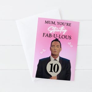 May include: A pink greeting card with the text "MUM, YOU'RE Strictly FAB-U-LOUS". The card features an illustration of a man holding a sign with the number 10. Two small pink hearts are on the left and right side of the card. Includes a white envelope.