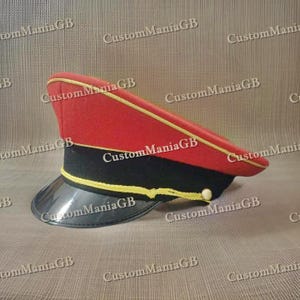 May include: A red and black military style hat with a gold trim. The hat has a black visor and a red crown with a gold band.