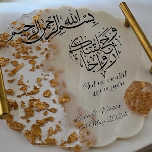 Puede incluir: Bandeja de resina blanca con motas doradas y un corazón de resina transparente. La bandeja tiene dos asas doradas y presenta caligrafía árabe y el texto "And we created you in pairs." La bandeja también incluye los nombres "Esha & Wasim" y la fecha "04 de mayo de 2024".