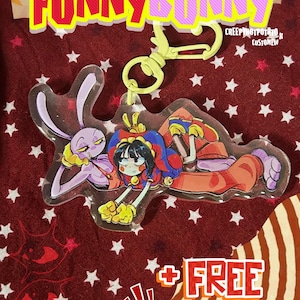 May include: An acrylic keyring featuring a purple rabbit character and a jester character with black hair, wearing a red and blue outfit. The keyring has a light yellow plastic clasp. Text on the image reads KEYCHAIN FUNNY BUNNY and FREE STICKER.