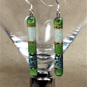 May include: A pair of green and white glass earrings with gold accents. The earrings are suspended from silver hooks.