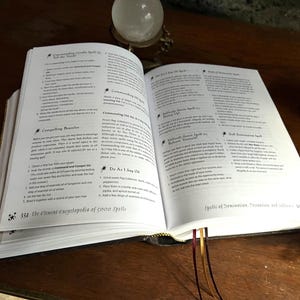 K&ouml;nnte beinhalten: Offenes Buch mit wei&szlig;en Seiten und schwarzem Text. Das Buch tr&auml;gt den Titel "The Element Encyclopedia of 5000 Spells". Das Buch ist auf einer Seite mit der &Uuml;berschrift "Spells of Domination, Persuasion and Influence" aufgeschlagen.