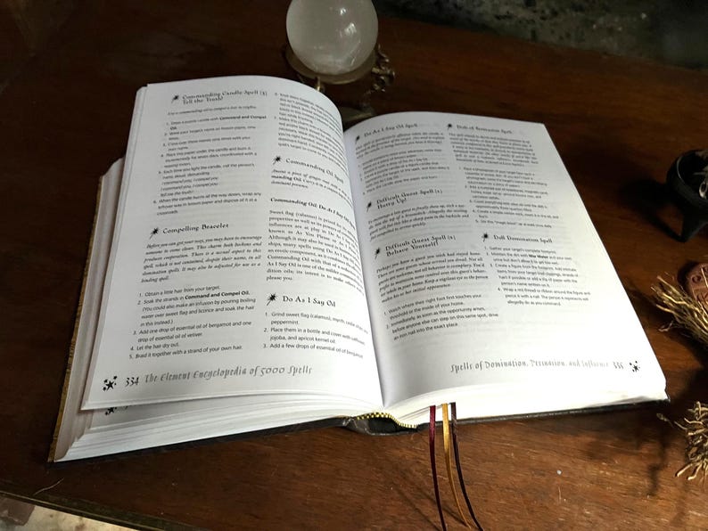 K&ouml;nnte beinhalten: Offenes Buch mit wei&szlig;en Seiten und schwarzem Text. Das Buch tr&auml;gt den Titel "The Element Encyclopedia of 5000 Spells". Das Buch ist auf einer Seite mit der &Uuml;berschrift "Spells of Domination, Persuasion and Influence" aufgeschlagen.
