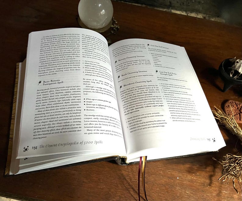 K&ouml;nnte beinhalten: Offenes Buch mit wei&szlig;en Seiten und schwarzem Text. Das Buch tr&auml;gt den Titel "The Element Encyclopedia of 5000 Spells". Das Buch ist auf einer Seite &uuml;ber "Basic Botany Fumigation Spell" und "Mandrake Cleansing Spell" ge&ouml;ffnet.