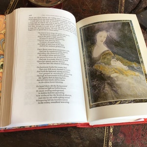 Puede incluir: Un libro abierto con una cubierta roja y p&aacute;ginas de guarda con vetas. El libro est&aacute; abierto en una p&aacute;gina con texto sobre los elfos y una ilustraci&oacute;n de acuarela de una mujer con un vestido fluido. El texto dice "La Comunidad del Anillo" e incluye un poema sobre los elfos.