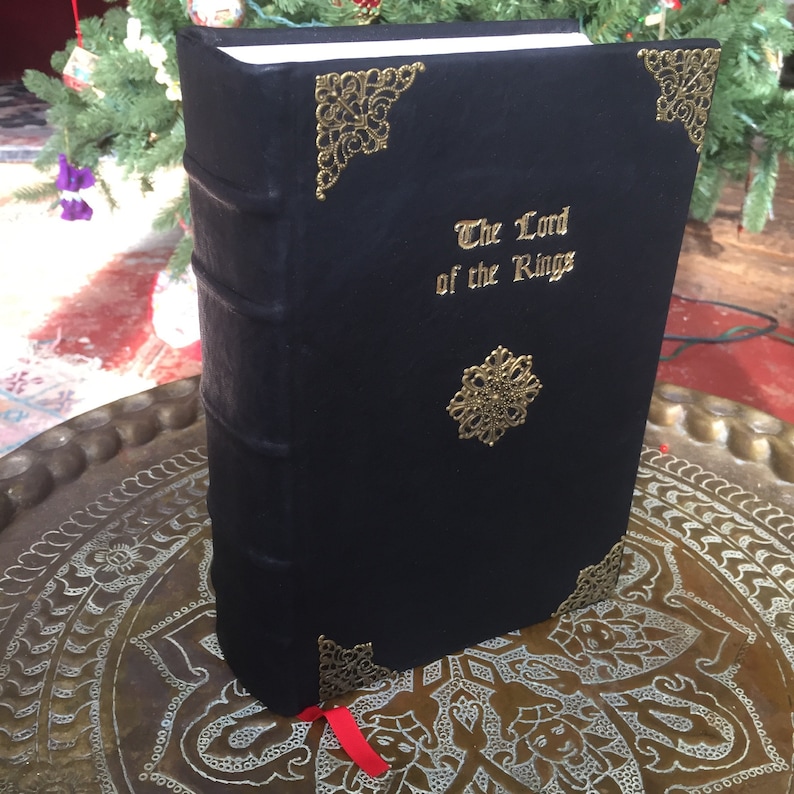 Puede incluir: Un libro encuadernado en cuero negro con letras doradas y detalles decorativos. El t&iacute;tulo de la portada dice "El Se&ntilde;or de los Anillos".