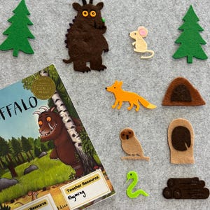 May include: A felt board featuring characters from "The Gruffalo" book. Includes a brown Gruffalo, a mouse, a fox, an owl, a snake, trees, and a book. The book cover is visible with the title "Gruffalo". The board also has the words "Teacher Resource" and "Rhyming".