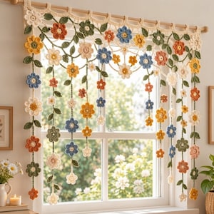 May include: A crochet window valance featuring a cream-coloured top border with hanging vertical strands of multi-coloured flowers and green leaves. The flowers are in shades of blue, orange, yellow, and white, creating a floral garland effect.
