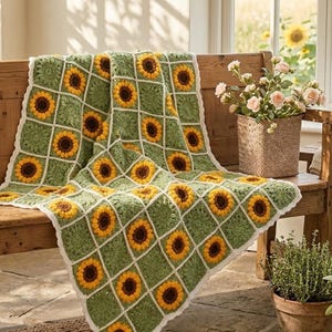 May include: A handmade crochet blanket featuring a grid of square motifs, each displaying a yellow and brown sunflower design on a textured sage green background, all bordered by a thin white yarn lattice and a scalloped white edge finish.