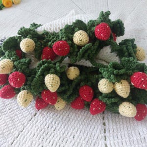May include: A crocheted garland featuring red and yellow strawberries with green leaves. The garland is made of yarn and is perfect for decorating a home or party.