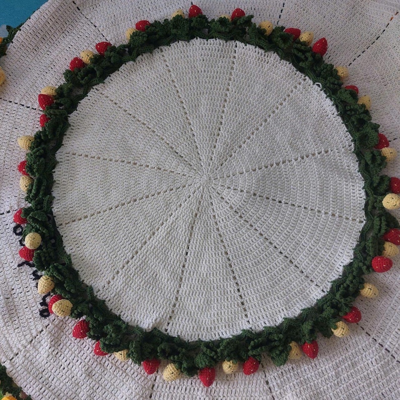May include: A white crocheted round tablecloth with a green and red strawberry border.