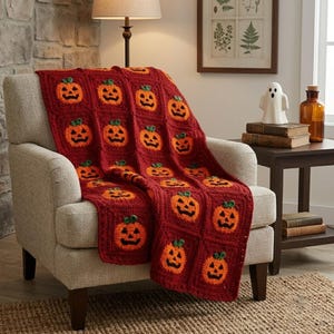 May include: A handmade crochet blanket featuring a repeating pattern of orange jack-o'-lantern squares on a deep red background. Each square displays a pumpkin with a black stitched face and a small green stem, creating a textured, square-grid design.