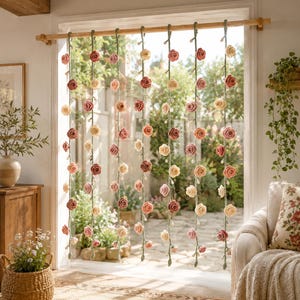May include: A decorative hanging curtain featuring seven vertical green crocheted vines adorned with numerous small, three-dimensional fabric roses in shades of cream, soft pink, and dusty rose, suspended from a horizontal wooden rod in a doorway.
