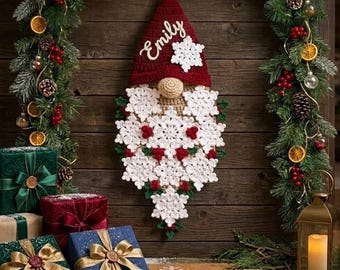May include: A crocheted gnome wall hanging featuring a dark red pointed hat with the name Emily embroidered in white script, a tan nose, and a long beard constructed from multiple white crocheted snowflakes with small red berry accents.