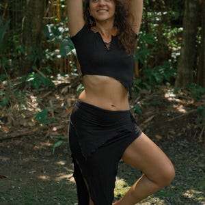 May include: A black short-sleeved crop top with a lace-up neckline and a matching black wrap skirt featuring an asymmetrical, jagged hemline. The fabric has a textured, crinkled appearance, and the garments are worn together as a coordinated set.