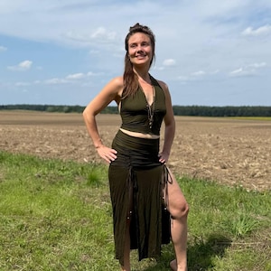 May include: An olive green halter top and skirt co-ord. The top has a halter neck and a necklace. The skirt has a high waist and a side split with drawstring details. The outfit is made of a soft, flowing fabric, suitable for warm weather.