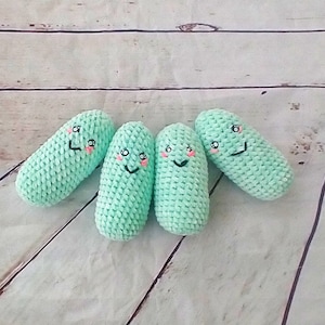 May include: Four crocheted green plush toys shaped like cucumbers with smiling faces. Each cucumber has pink cheeks and black eyes.