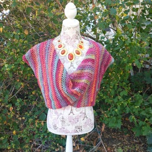 May include: A colorful striped crochet top with a cowl neck and short sleeves. The top is displayed on a white mannequin with a gold and red beaded necklace.