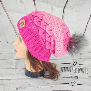 May include: A pink and white ombre crochet beanie with a faux fur pom pom and a sparkly embellishment. The beanie is on a mannequin head with long brown hair.