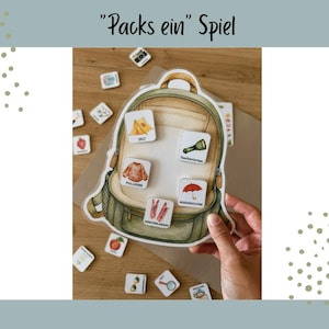 Könnte beinhalten: Ein Spiel mit dem Titel Packs ein Spiel, bestehend aus einem großen illustrierten grünen Rucksack-Ausschnitt. Auf dem Rucksack sind fünf quadratische Kärtchen mit Abbildungen von Zelt, Taschenlampe, Pullover, Regenschirm und Wäscheklammern befestigt.