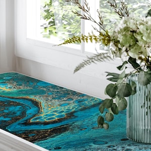 May include: A windowsill with a decorative vinyl sticker featuring a blue, green, and gold abstract design. The sticker is placed on a white windowsill with a vase of white flowers on the right side.