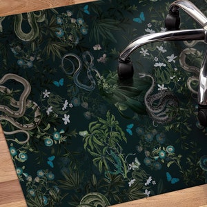 Könnte beinhalten: Eine dunkelgrüne und schwarze gemusterte Fußmatte mit einem Design aus Schlangen, Schmetterlingen und Blumen. Die Matte ist so konzipiert, dass sie Böden vor Stuhlrollen schützt.