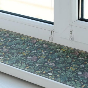 May include: A white window sill with a floral patterned vinyl covering. The vinyl has a dark green background with small white, pink, and yellow flowers.