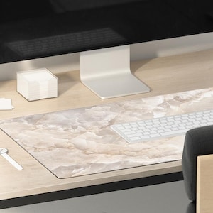 May include: A light wood desk with a black metal frame. A white computer monitor, a white keyboard, a white mouse, a small potted plant, a white watch, a white cube, and a clear glass cup with a pencil are on the desk. A black and gray chair is in the background.