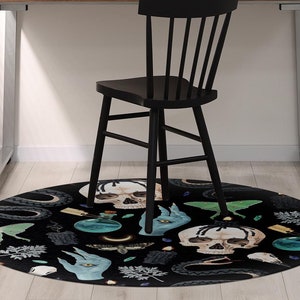 Peut inclure: Un tapis rond noir et vert avec un motif effrayant et occulte représentant des crânes, des yeux, des serpents et d'autres symboles mystiques. Le tapis est placé sous une chaise noire dans un bureau à domicile.