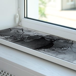 Puede incluir: Un alféizar de ventana blanco con un diseño abstracto en blanco y negro en la superficie. El diseño presenta patrones en espiral y toques de purpurina plateada.