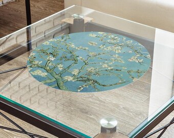 May include: A glass coffee table with a black metal frame and wooden legs. The table has a round, blue and white floral print coaster on top.