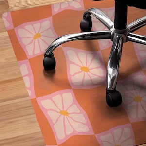 May include: A pink and orange checkered floor mat with white daisy designs. The mat is designed to protect floors from rolling office chair wheels.