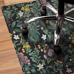 May include: A black and green floral patterned chair mat with a silver office chair on top of it. The chair mat is on a wood floor.