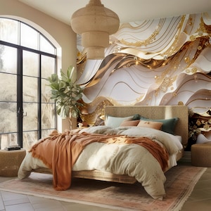 Puede incluir: Un dormitorio con una cama que tiene una cabecera tejida y un papel tapiz con estampado blanco y dorado. La cama está hecha con un edredón blanco, una manta de tiro marrón y algunas almohadas. Hay una mesa pequeña con una planta al lado de la cama.